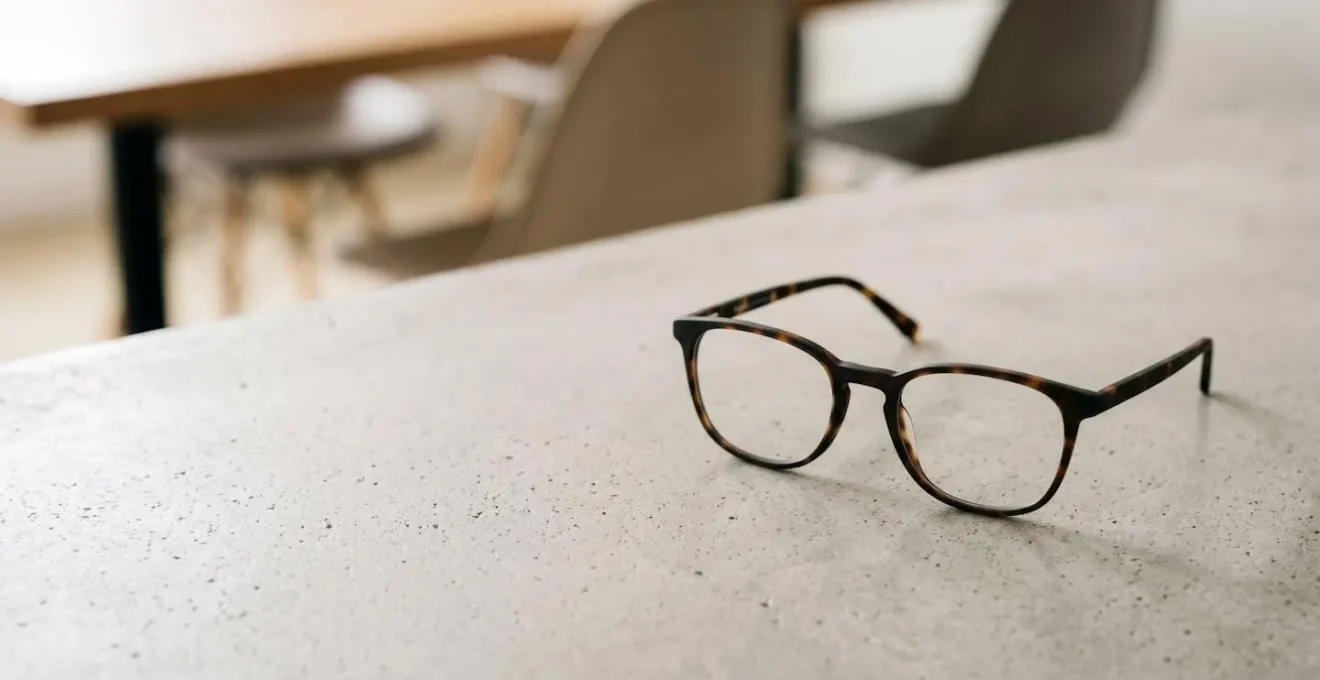 Paire de lunettes élégante posée sur une table avec lumière naturelle douce symbolisant l'accessibilité des soins optiques