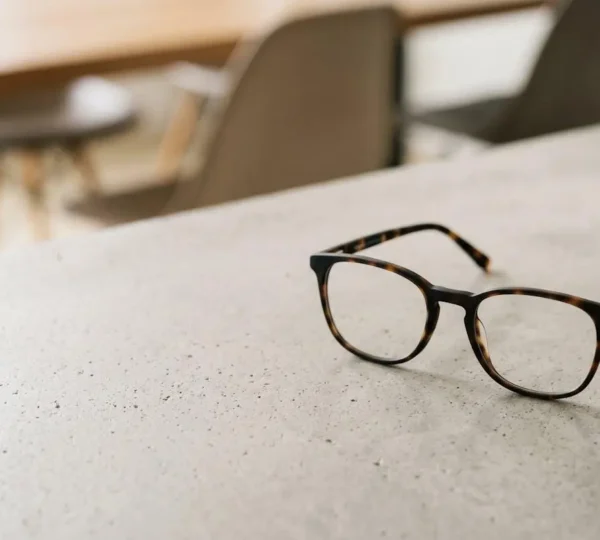 Paire de lunettes élégante posée sur une table avec lumière naturelle douce symbolisant l'accessibilité des soins optiques